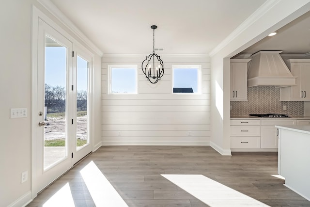 unfurnished dining area featuring a healthy amount of sunlight, wood-type flooring, wooden walls, and a chandelier