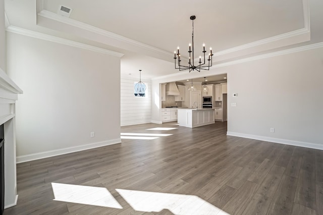 unfurnished living room featuring a raised ceiling, dark hardwood / wood-style flooring, crown molding, and a notable chandelier