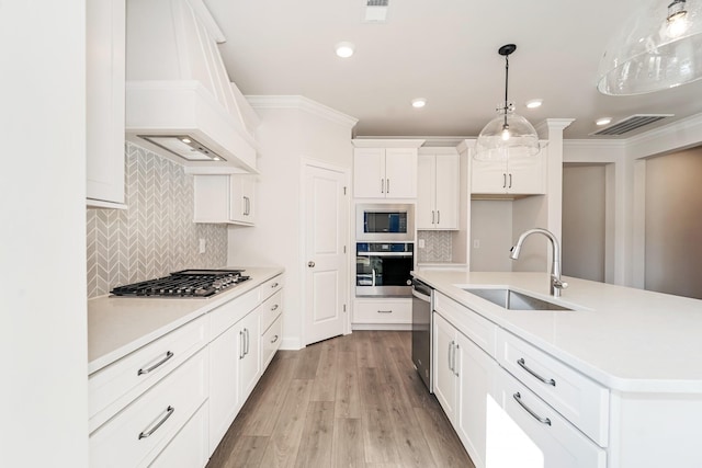 kitchen with pendant lighting, a center island with sink, sink, light hardwood / wood-style flooring, and appliances with stainless steel finishes