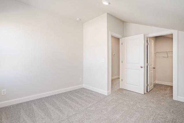 unfurnished bedroom with lofted ceiling, a spacious closet, light carpet, and a closet