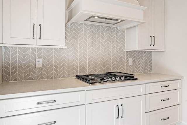 kitchen featuring stainless steel gas stovetop, decorative backsplash, white cabinets, and custom exhaust hood