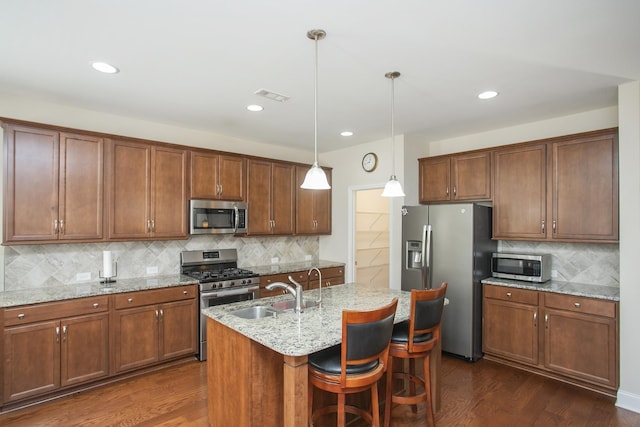 kitchen with pendant lighting, a center island with sink, stainless steel appliances, and dark wood-type flooring