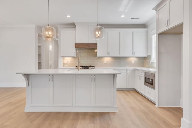 kitchen featuring white cabinetry, a center island with sink, hanging light fixtures, and light hardwood / wood-style flooring