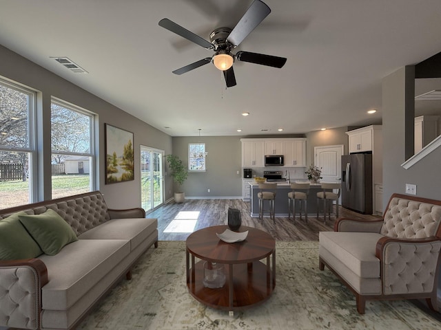 living room with light wood-type flooring, ceiling fan, and a healthy amount of sunlight