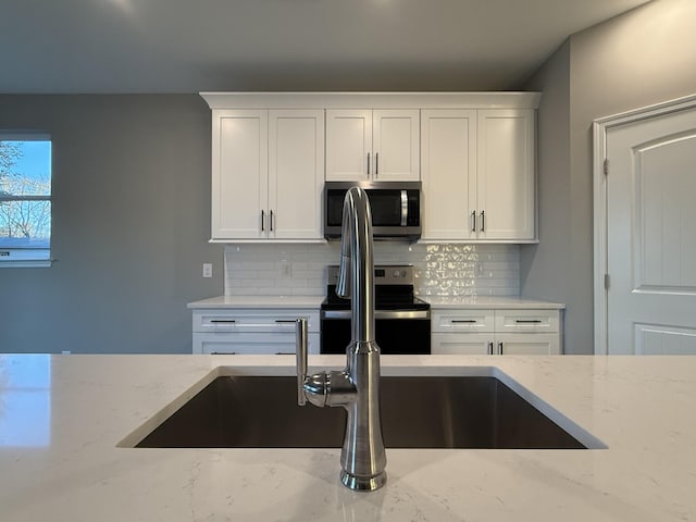 kitchen featuring white cabinetry, backsplash, light stone countertops, and stainless steel appliances