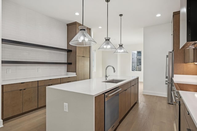 kitchen featuring a kitchen island with sink, hanging light fixtures, sink, light hardwood / wood-style flooring, and stainless steel appliances