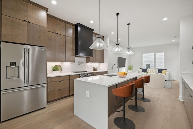 kitchen featuring appliances with stainless steel finishes, sink, custom range hood, a kitchen breakfast bar, and an island with sink