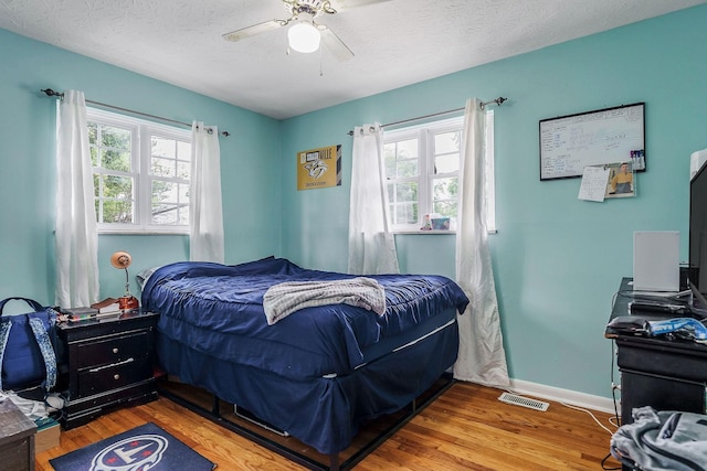 bedroom featuring multiple windows, hardwood / wood-style floors, a textured ceiling, and ceiling fan