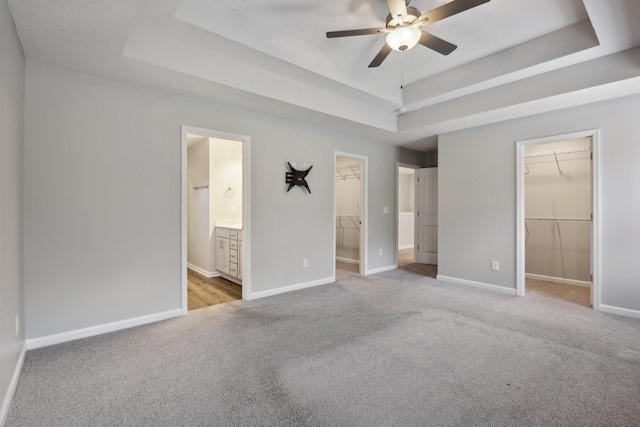 unfurnished bedroom featuring light carpet, a walk in closet, ensuite bath, a raised ceiling, and ceiling fan