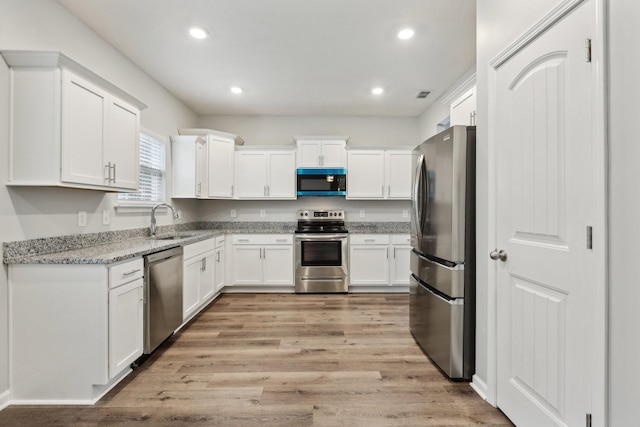 kitchen featuring light stone counters, stainless steel appliances, sink, light hardwood / wood-style flooring, and white cabinets