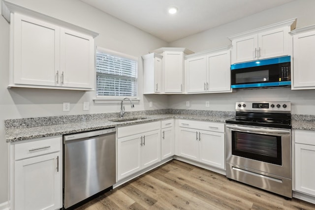 kitchen with light stone countertops, stainless steel appliances, sink, light hardwood / wood-style floors, and white cabinetry