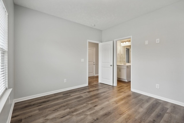 unfurnished bedroom with ensuite bathroom and dark wood-type flooring