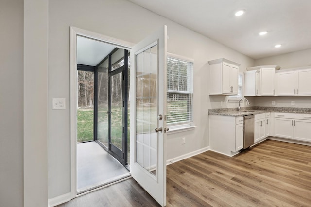 kitchen featuring dishwasher, sink, light stone counters, hardwood / wood-style floors, and white cabinets