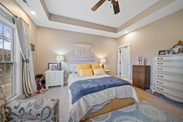 bedroom with a raised ceiling, ceiling fan, and light colored carpet