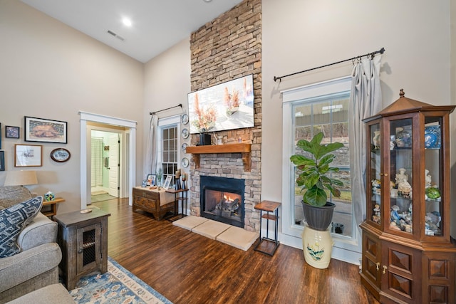 living room featuring a stone fireplace, dark hardwood / wood-style flooring, and a towering ceiling