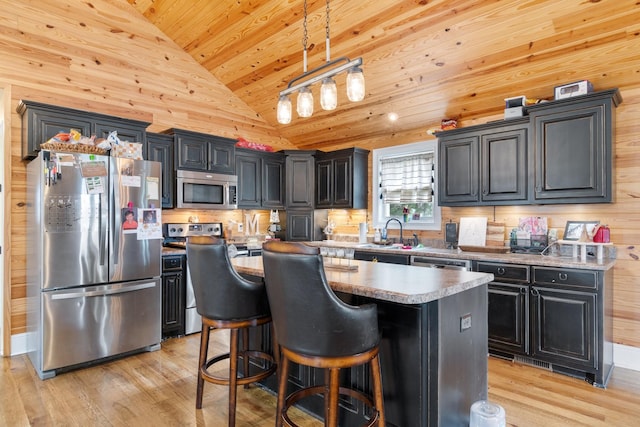 kitchen with appliances with stainless steel finishes, light wood-type flooring, decorative light fixtures, and a kitchen island