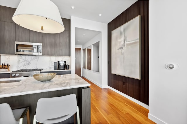 kitchen featuring light stone counters, range, decorative backsplash, a kitchen bar, and light wood-type flooring