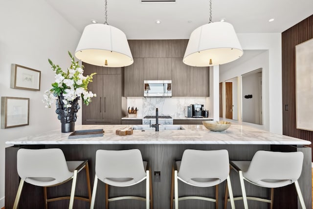 kitchen with a large island with sink, a breakfast bar, decorative backsplash, and pendant lighting