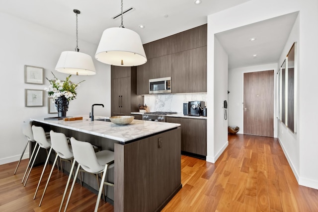 kitchen featuring a kitchen bar, light hardwood / wood-style floors, stove, decorative backsplash, and hanging light fixtures