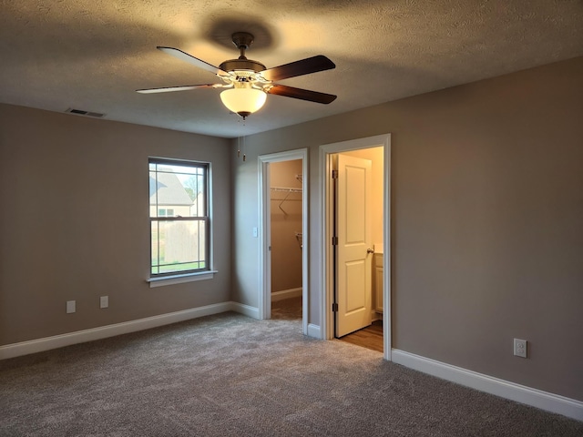 unfurnished bedroom with a textured ceiling, a walk in closet, a closet, carpet flooring, and ceiling fan