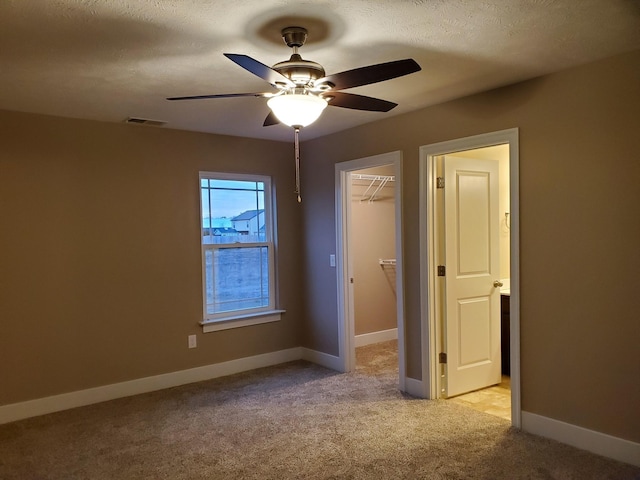 unfurnished bedroom with ceiling fan, light colored carpet, a spacious closet, a textured ceiling, and a closet