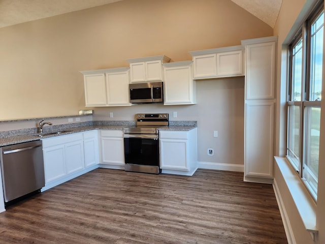 kitchen with light stone countertops, white cabinets, appliances with stainless steel finishes, sink, and vaulted ceiling