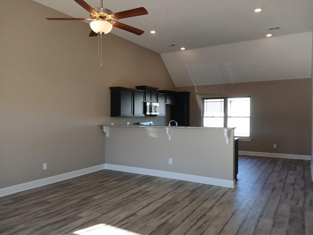 kitchen featuring ceiling fan, vaulted ceiling, kitchen peninsula, dark wood-type flooring, and a breakfast bar area