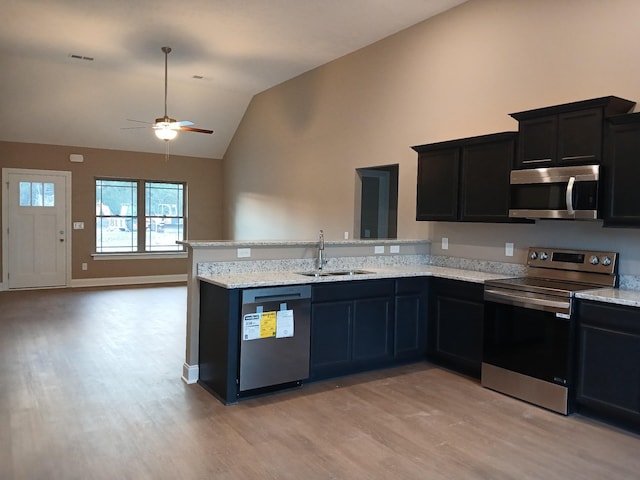 kitchen with vaulted ceiling, light hardwood / wood-style floors, sink, light stone countertops, and appliances with stainless steel finishes