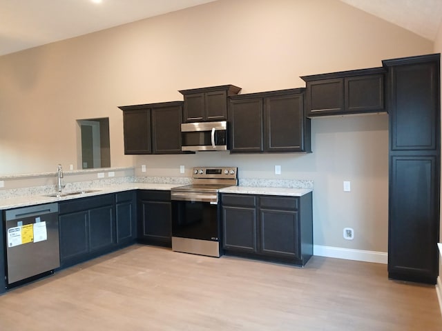 kitchen featuring stainless steel appliances, lofted ceiling, light hardwood / wood-style flooring, and sink