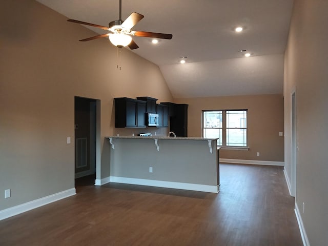 kitchen with high vaulted ceiling, kitchen peninsula, dark wood-type flooring, and a kitchen breakfast bar