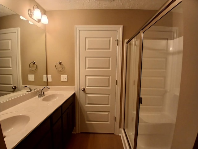 bathroom featuring a textured ceiling, hardwood / wood-style floors, a shower with door, and vanity