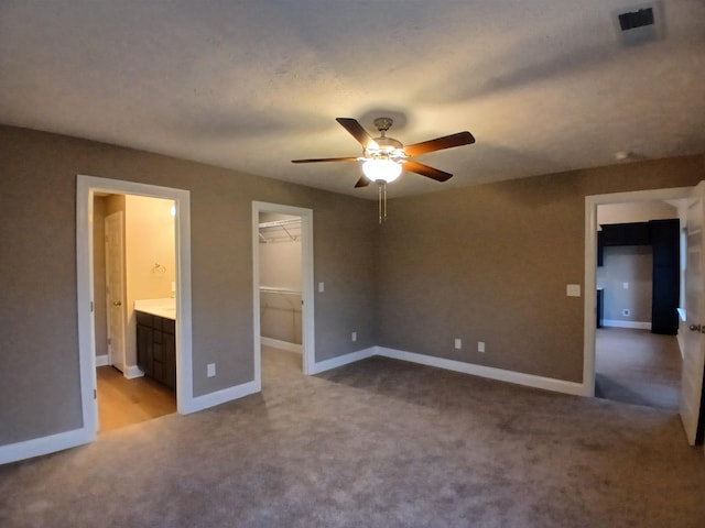 unfurnished bedroom featuring ceiling fan, carpet, a spacious closet, connected bathroom, and a closet