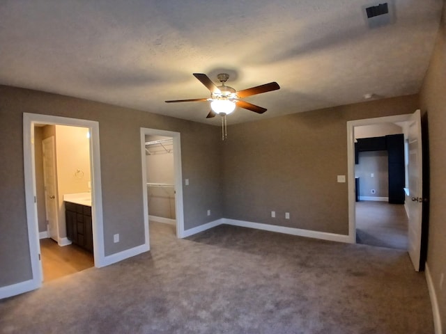 unfurnished bedroom featuring ceiling fan, ensuite bath, light carpet, a walk in closet, and a closet