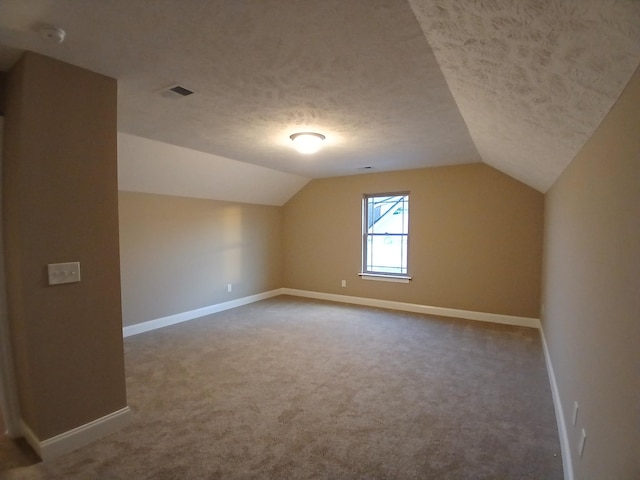 additional living space with vaulted ceiling, a textured ceiling, and carpet flooring