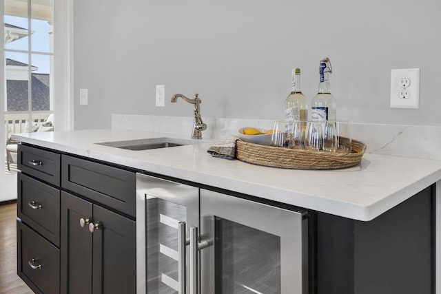 kitchen with light stone countertops, sink, beverage cooler, and light hardwood / wood-style flooring