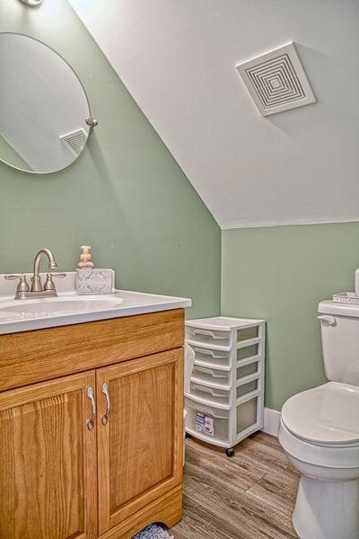 bathroom with toilet, vanity, lofted ceiling, and hardwood / wood-style flooring