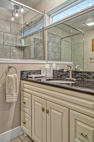 bathroom featuring tile patterned floors, decorative backsplash, an enclosed shower, and vanity