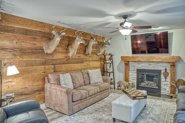 living room featuring hardwood / wood-style floors, ceiling fan, and a stone fireplace