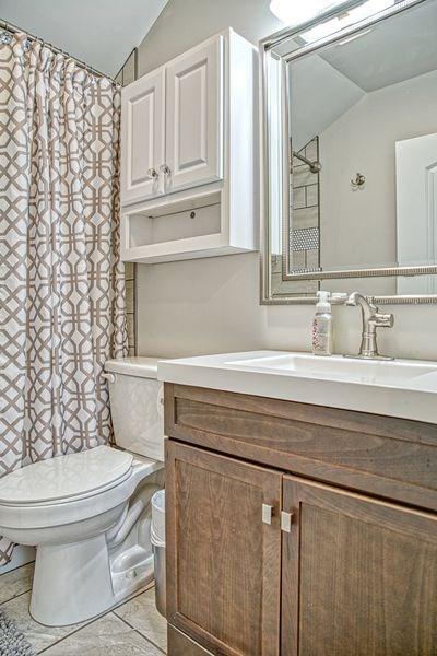 bathroom featuring tile patterned flooring, vanity, toilet, and lofted ceiling