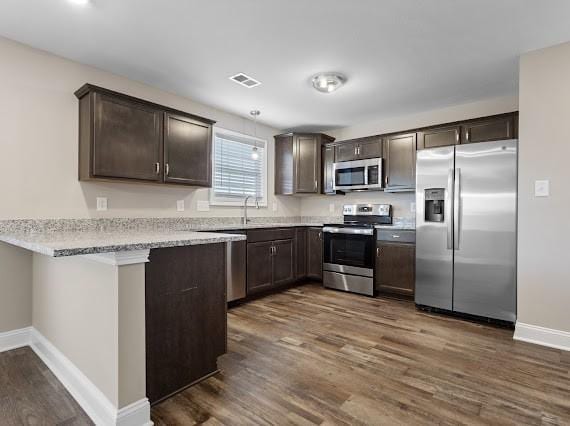 kitchen featuring pendant lighting, dark wood-type flooring, dark brown cabinets, stainless steel appliances, and kitchen peninsula