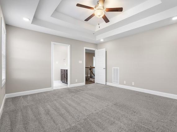 spare room with light colored carpet, a raised ceiling, and ceiling fan