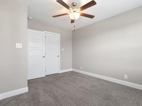 unfurnished bedroom featuring dark colored carpet, ceiling fan, and a closet