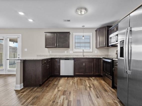 kitchen with dark brown cabinets, hanging light fixtures, appliances with stainless steel finishes, kitchen peninsula, and hardwood / wood-style flooring