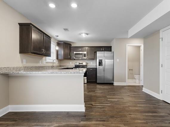 kitchen featuring appliances with stainless steel finishes, dark hardwood / wood-style floors, light stone counters, and dark brown cabinetry