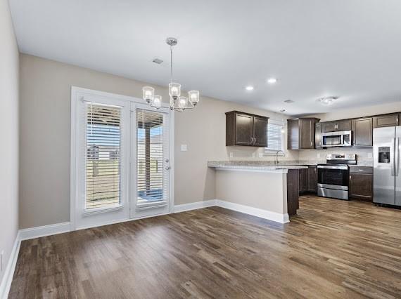 kitchen with appliances with stainless steel finishes, a wealth of natural light, dark brown cabinetry, and kitchen peninsula