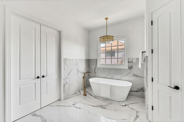 bathroom featuring a washtub, a chandelier, and tile walls