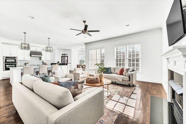 living room featuring ceiling fan with notable chandelier, ornamental molding, and dark wood-type flooring