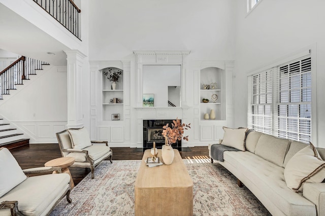 living room featuring built in shelves, hardwood / wood-style floors, a towering ceiling, and ornate columns