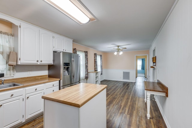 kitchen with stainless steel refrigerator with ice dispenser, ceiling fan, ornamental molding, a kitchen island, and white cabinetry