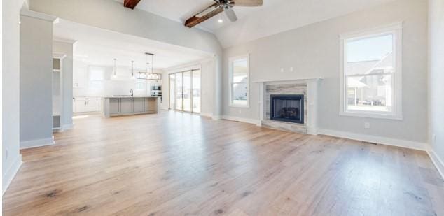 unfurnished living room featuring plenty of natural light, light hardwood / wood-style floors, ceiling fan, and vaulted ceiling